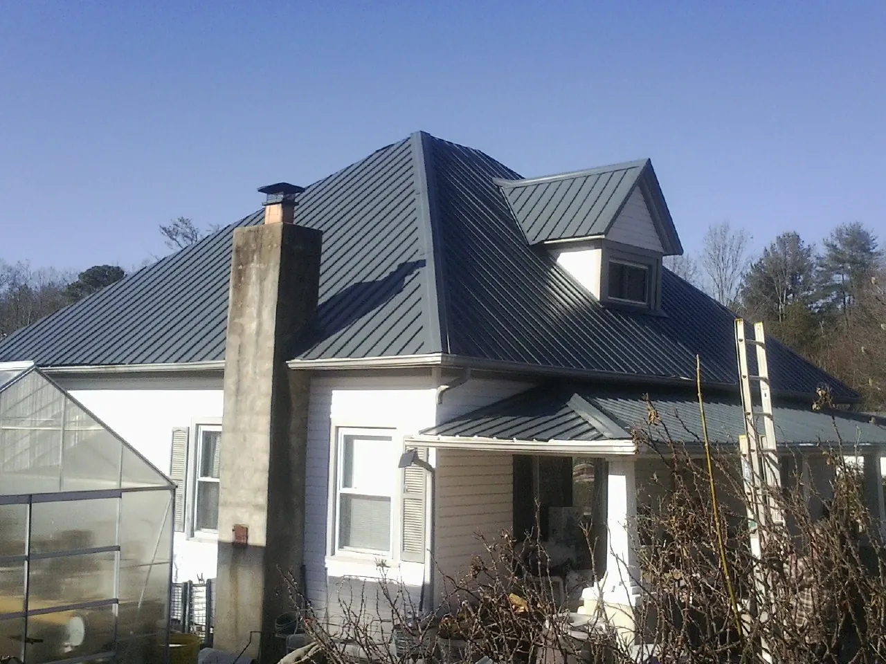 Dark blue standing seam metal roof on a white farmhouse with dormer — Slate & Tile Roof Repair by Roofing Brothers in Clearwater