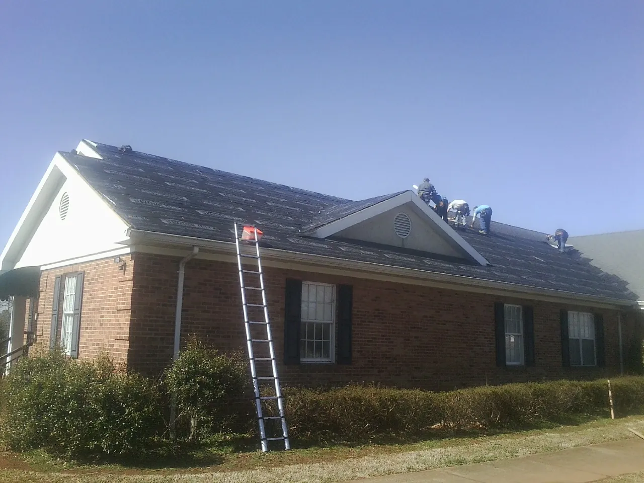 Crew tearing shingles off a brick ranch roof with a ladder set — Emergency Roof Repair work by our crew in Clearwater