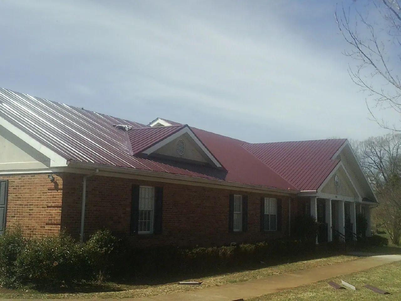 Red metal roof with gabled entries on a long brick building, from a Hail Damage Roof Repair job in Clearwater